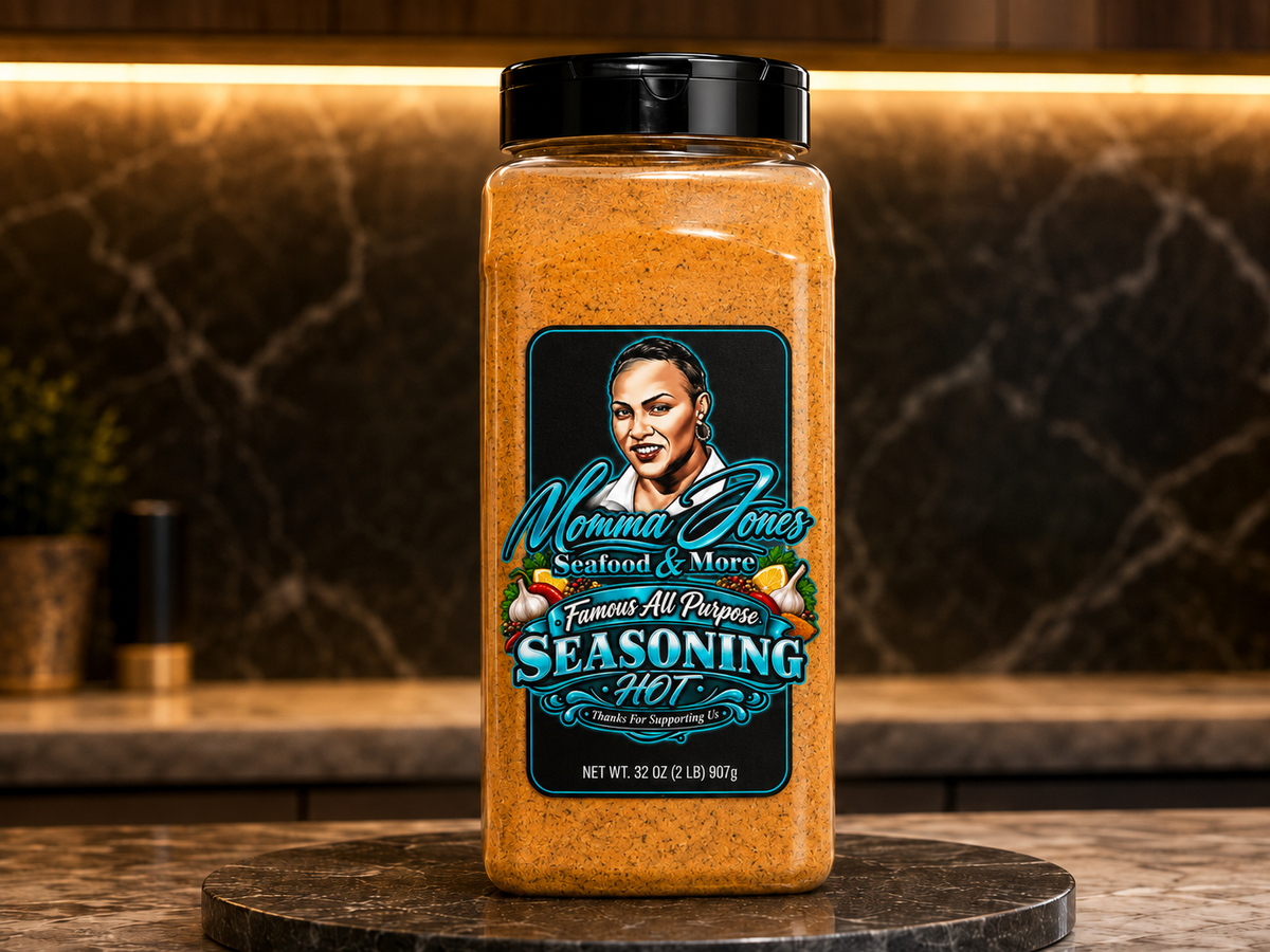 A large plastic jar of Momma Jones Seasoning Hot stands on a round stone pedestal in a kitchen setting with a dark marble backsplash and warm under-cabinet lighting.