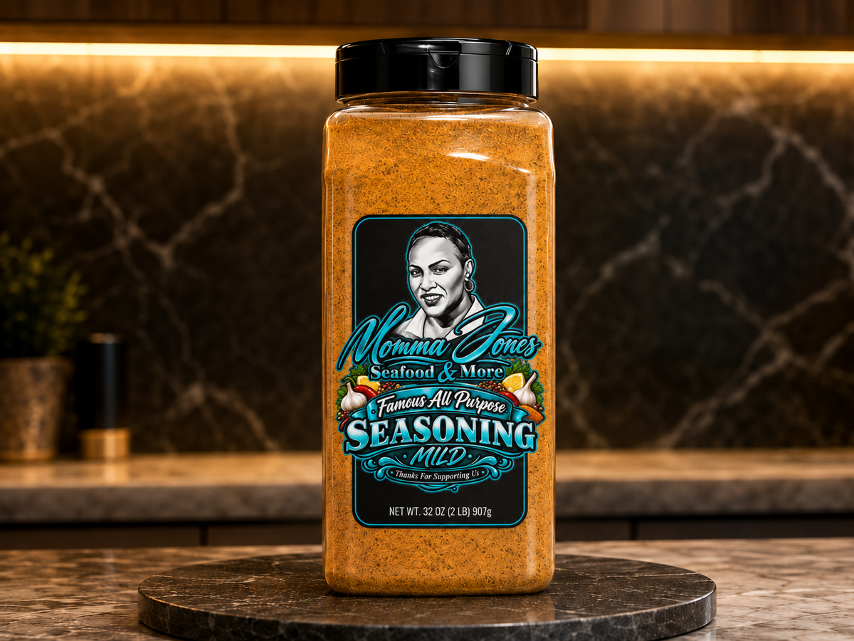 A large plastic jar of Momma Jones Seafood & More Seasoning, labeled 'Mild', displayed on a round stone coaster in a kitchen setting with a dark marble backsplash.