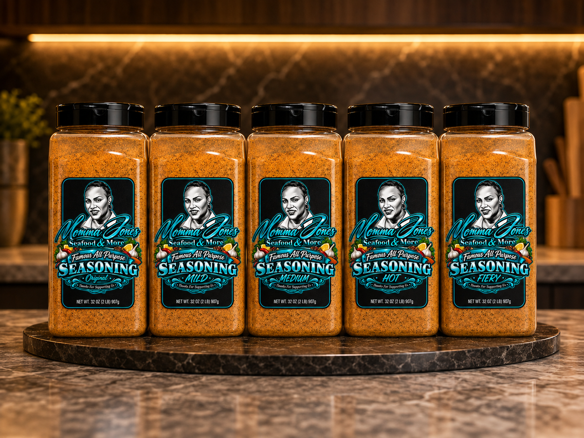 Five clear plastic jars of Momma Jones Jar Seasoning blend filled with orange-brown seasoning, arranged on a round dark marble tray against a warm, blurred kitchen background.